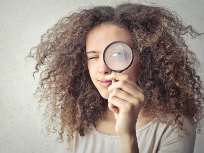 portrait photo of woman holding up a magnifying glass over her eye